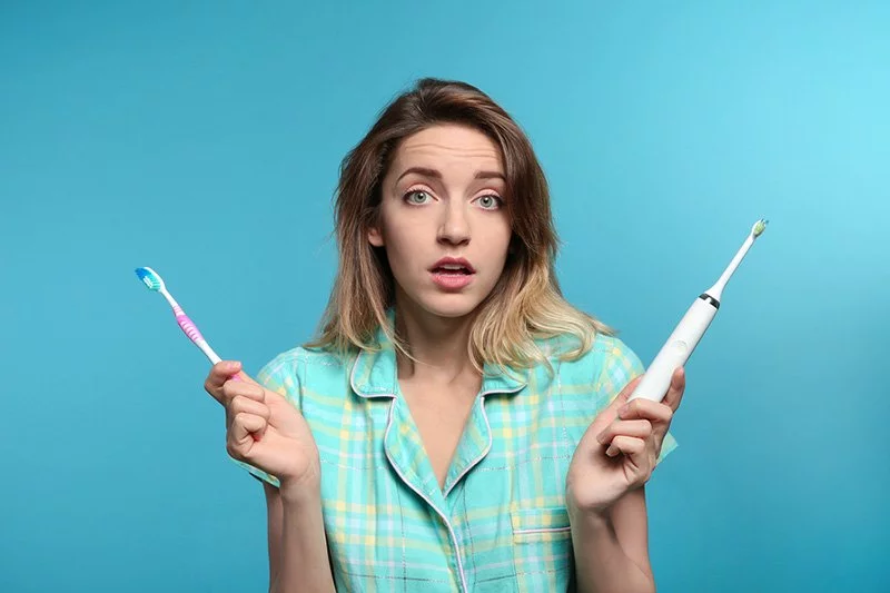 Young woman choosing between manual and electric toothbrushes.