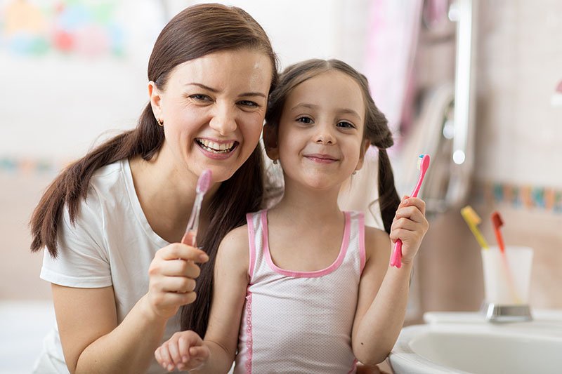 Smiling mom and child holding toothbrushes